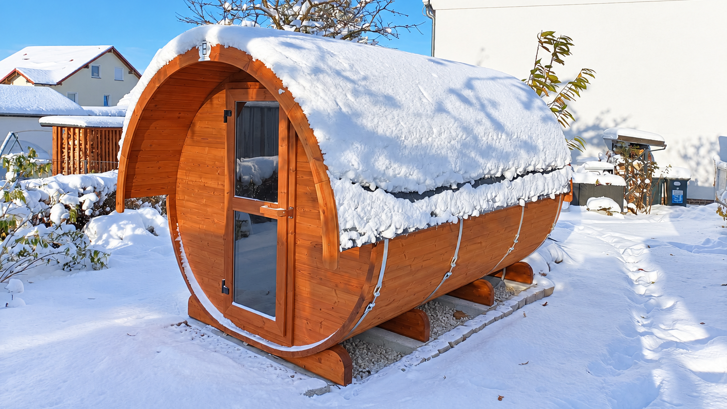 FassSauna Suuri mit Vorraum aus Thermoholz mit verschneitem Runddach und Glastür in einem winterlichen Garten
